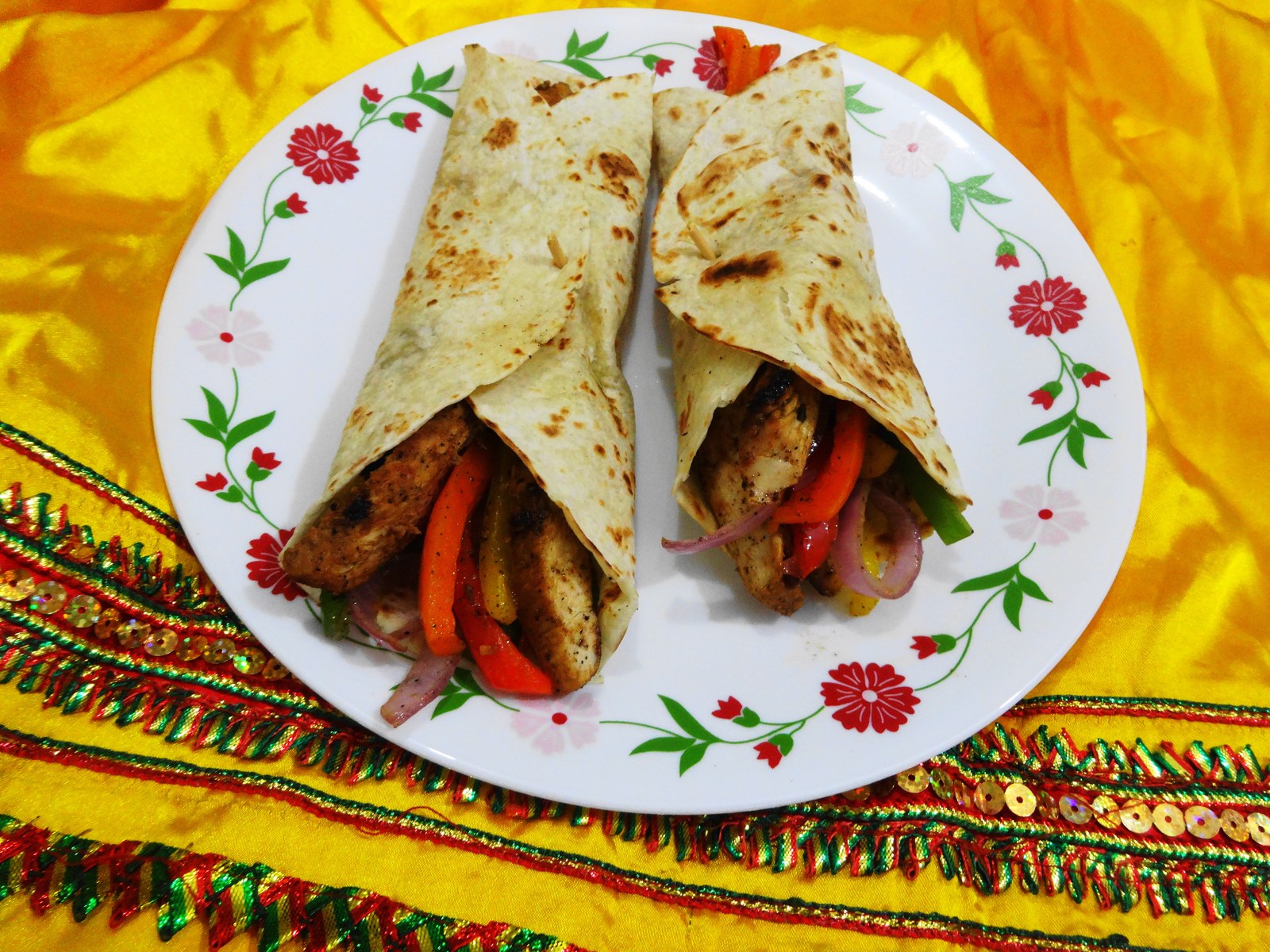 Two fajita wraps on a plate placed on decorated cloth